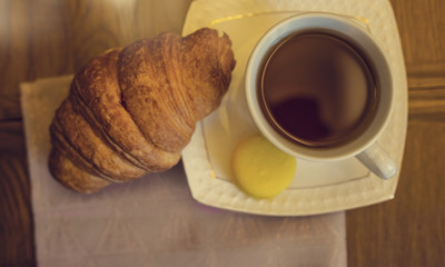 Delicious croissant with cup of coffee on wooden board