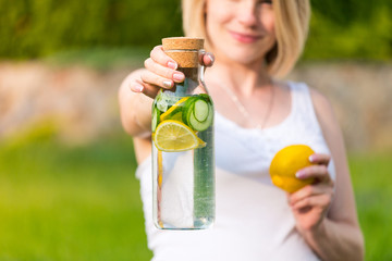 healthy eating, drinks, diet. The girl is holding a detox drink from a lemon and mint with a cucumber on a background of green grass