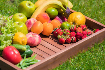Various vegetables and fruits on a wooden tray against a background of green grass