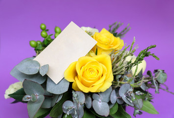 Festive flower arrangement of yellow roses and other plants with clear card for text on violet background.