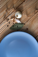 Fototapeta na wymiar onion, garlic, black pepper and bay leaf with empty blue plate on a wooden background