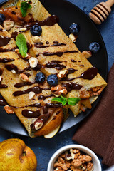 Homemade thin pancakes with caramelized pears, chocolate sauce and nuts on a concrete background.