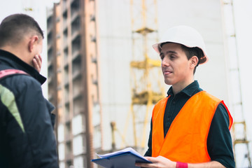 Builder in helmet showing tongue holds documents on building