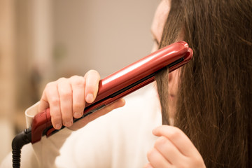 Pretty young brunette woman ironing the hair by professional curling iron