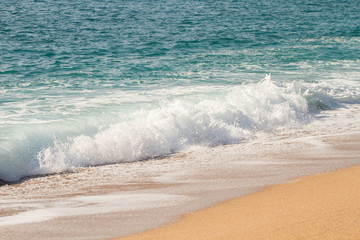 A blue wave runs across the sandy beach of Spain at noon