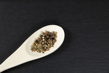 Wooden spoon with black pepper on black background