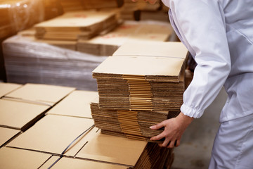 Close up of young female worker picking up stacks of folded cardboard boxes from a bigger stack in...
