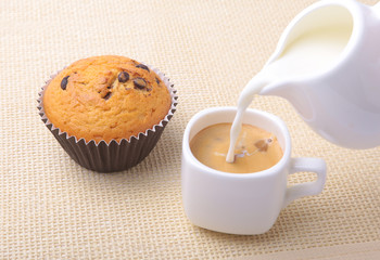 Perfect morning breakfast with Delicious homemade cupcakes with raisins, chocolate chips, espresso coffee in white cup and milk on textile background. Muffins.