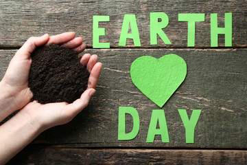 Female hands holding ground with inscription Earth Day on wooden table