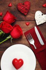 Red heart on white plate with kitchen cutlery and red roses on wooden table