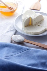 Cheese, honey and sour cream, feta in a white plate, soft cheese on a white background, wooden spoon with sour cream, French breakfast, blue napkin, honey in glassware, blank for designer