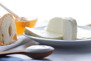 Cheese, honey and sour cream, feta in a white plate, soft cheese on a white background, wooden spoon with sour cream, French breakfast, blue napkin, honey in glassware, blank for designer