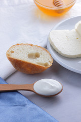 Fototapeta na wymiar Cheese, honey and sour cream, feta in a white plate, soft cheese on a white background, wooden spoon with sour cream, French breakfast, blue napkin, honey in glassware, blank for designer
