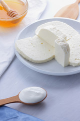 Cheese, honey and sour cream, feta in a white plate, soft cheese on a white background, wooden spoon with sour cream, French breakfast, blue napkin, honey in glassware, blank for designer