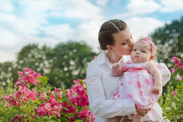 Young beautiful mother holding a small daughter in her arms in a garden with roses
