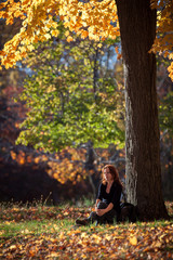 Melancholic woman rests under a tree. Warm afternoon light glows through the fall foliage, in Ringwood state park, NJ