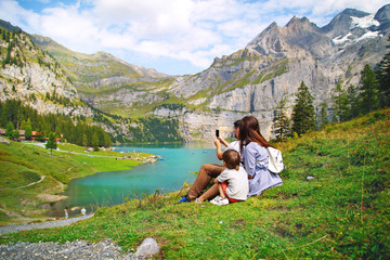 young happy family of tourists photographing nature, beautiful blue natural lake oeschinensee, in Switzerland, a fantastic mountain landscape overlooking the water and forest