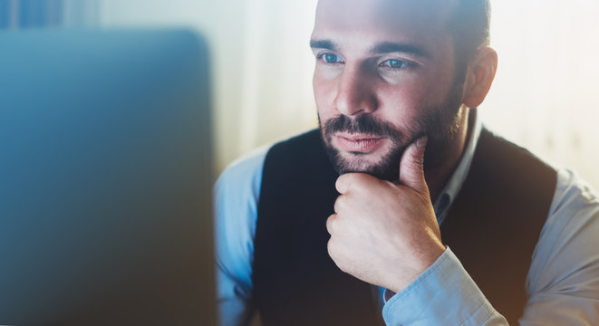 Bearded young businessman working on modern office. Consultant man thinking looking in monitor computer. Manager typing on keyboard in coworking workplace, startup project concept