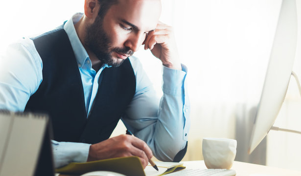 Bearded businessman working on modern office. Consultant man thinking looking in monitor computer. Manager writes in notebook in coworking workplace, startup project concept in studio