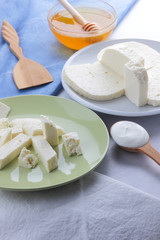 Cheese pattern, honey and sour cream, feta in white and green plate, soft cheese on a white background, wooden spoon with sour cream, French breakfast, blue napkin, honey in glassware
