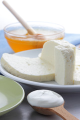 Cheese pattern, honey and sour cream, feta in white and green plate, soft cheese on a white background, wooden spoon with sour cream, French breakfast, blue napkin, honey in glassware