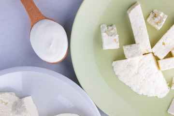 Cheese pattern, honey and sour cream, feta in white and green plate, soft cheese on a white background, wooden spoon with sour cream, French breakfast, blue napkin, honey in glassware