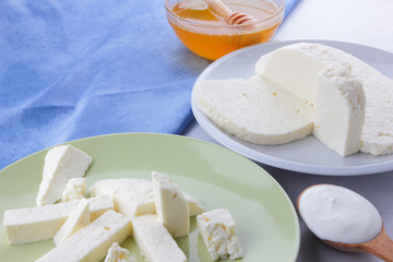 Cheese pattern, honey and sour cream, feta in white and green plate, soft cheese on a white background, wooden spoon with sour cream, French breakfast, blue napkin, honey in glassware
