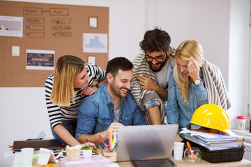 Young beautiful happy business team looking at laptop while laughing and brainstorming their ideas.