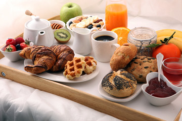 breakfast in bed with fruits and pastries on a tray -waffles, croissants, coffe and juice