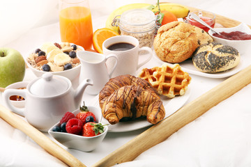 breakfast in bed with fruits and pastries on a tray -waffles, croissants, coffe and juice