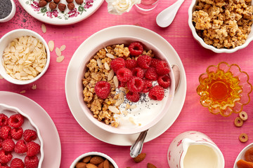 Granola with natural yogurt, fresh raspberries, honey, almond flakes, and poppy seeds in a ceramic bowl on a pink wooden table, top view. Delicious and nutritious breakfast or dessert. Healthy food.