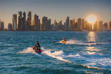 Fotobehang Two jet-skis cruising with the skyline of West Bay in background, seen at sunset from the Dhow Harbour. Doha, Qatar. © aspas