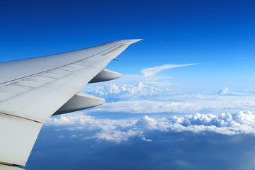 Fototapeta premium Aerial view of plane window above clouds under blue sky. View from aircraft window