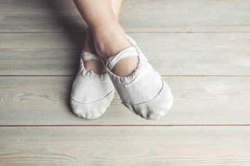 A little dancer. Legs of a girl in ballet slippers on a wooden floor