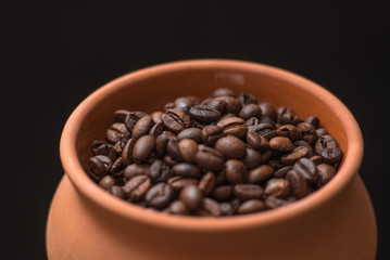 Clay pot filled with coffee beans on black background. Place for text