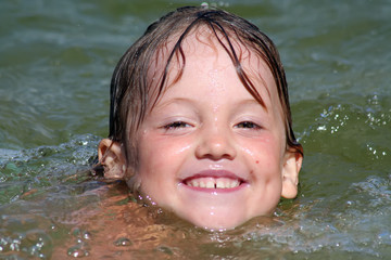 the head of a small smiling swiming girl above the surface of th