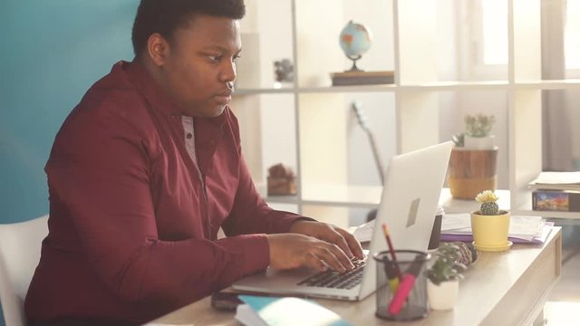 Serious young african american man thinking and working on laptop take documents in office sunlight business internet face businessman freelance looking portrait work slow motion black brainstorming