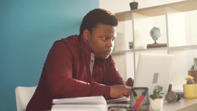 Concentrated young african american man writing and working on laptop in office sunlight business internet face businessman freelance looking portrait serious work slow motion black brainstorming