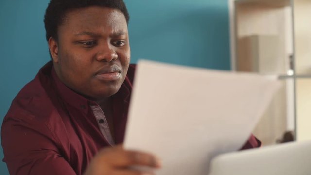 Close up face thinking young african american man writing and working on laptop in office sunlight business internet businessman freelance looking portrait serious work slow motion black brainstorming