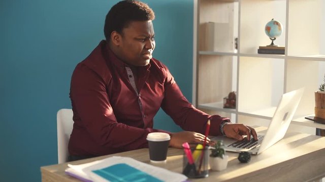 Nervous young african american man use laptop in office sunlight angry sad business internet face businessman freelance looking portrait serious work slow motion black brainstorming close up