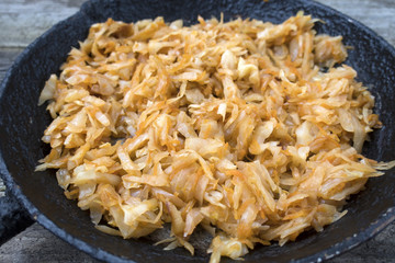 Appetizing fried cabbage in an old frying pan on an old wooden background close-up.