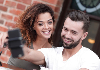 Happy cheerful couple sitting down at a cafe and making selfie