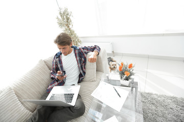 young man with laptop and smartphone sitting on sofa in living room.