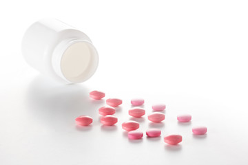 Heap of medical pills in red colors and plastic white bottle. Pills on white background. Concept of healthcare and medicine.