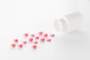 Heap of medical pills in red colors and plastic white bottle. Pills on white background. Concept of healthcare and medicine.
