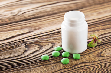 Medical herbal pills in green color and white bottle on wooden background. Concept of herbal healthcare and medicine.