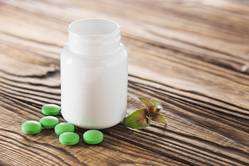 Medical herbal pills in green color and white bottle on wooden background. Concept of herbal healthcare and medicine.