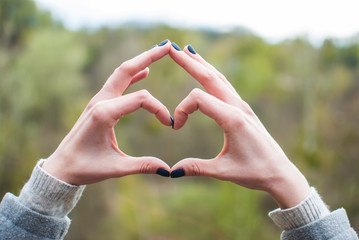 Tender girl's pale hands forming a heart shape gesture. Concept (idea) of love, friendship, romance, passion.