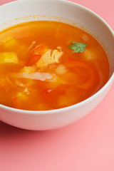 Hot vegetable soup with chicken meat in a bowl. a leaf of greenery. on a pink background. The concept of a healthy food and diet. Closeup.