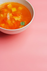 Hot vegetable soup with chicken meat in a bowl. a leaf of greenery. on a pink background. The concept of a healthy food and diet